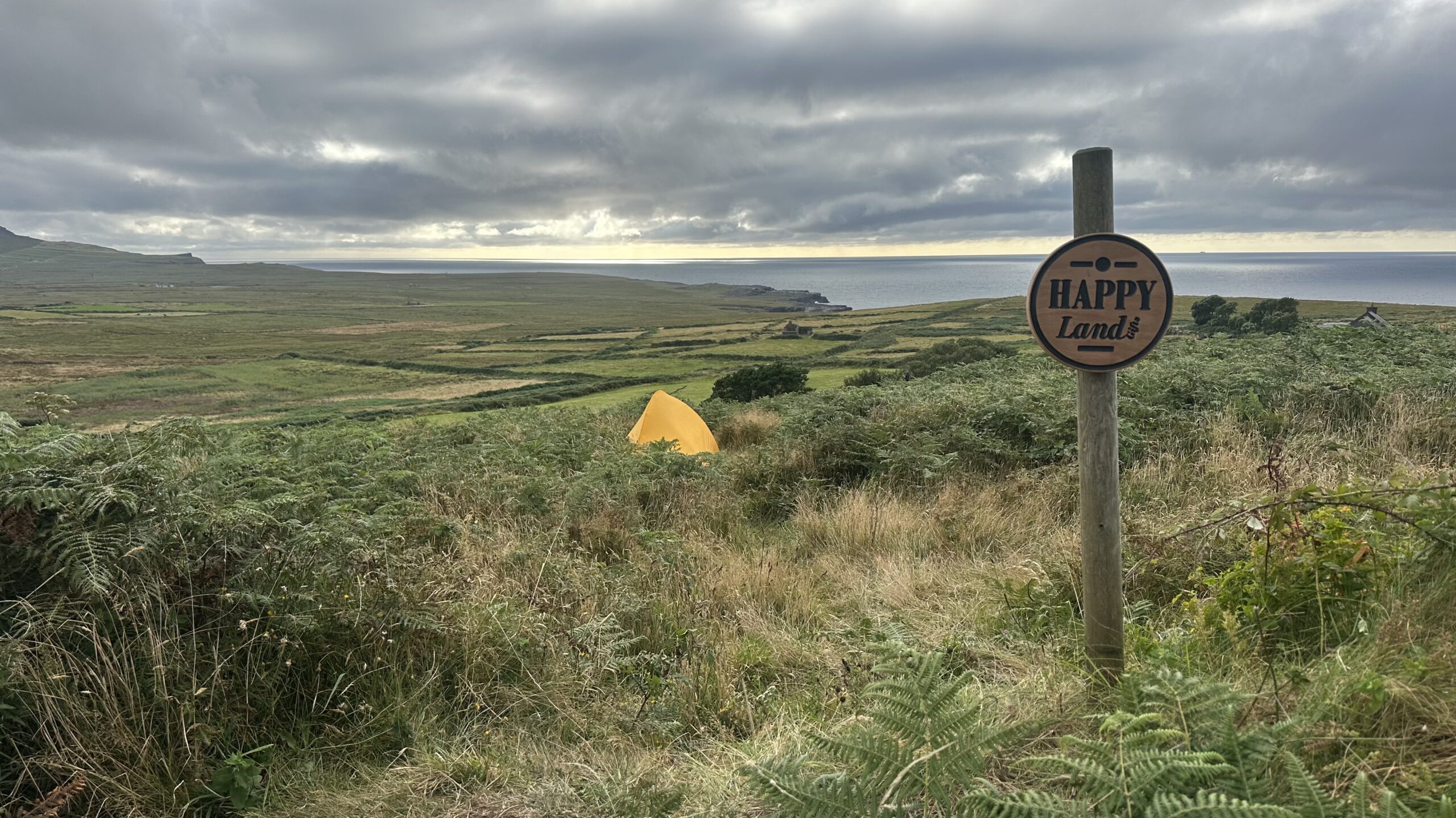 Our property in Ireland with a HappyLandGifts sign, a yellow tent, and a view of the Atlantic Ocean